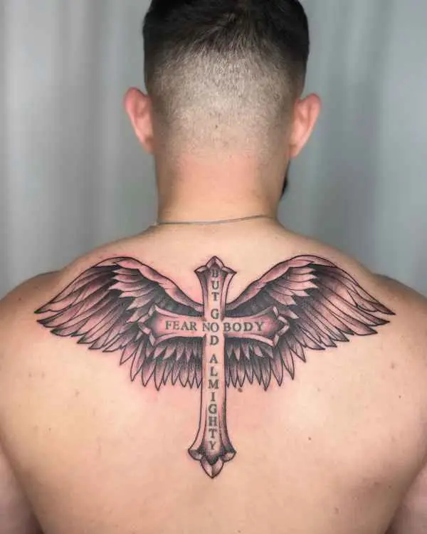 A black and grey winged cross tattoo on an upper back reading Fear No Body But God Almighty, by Jordan Joyes