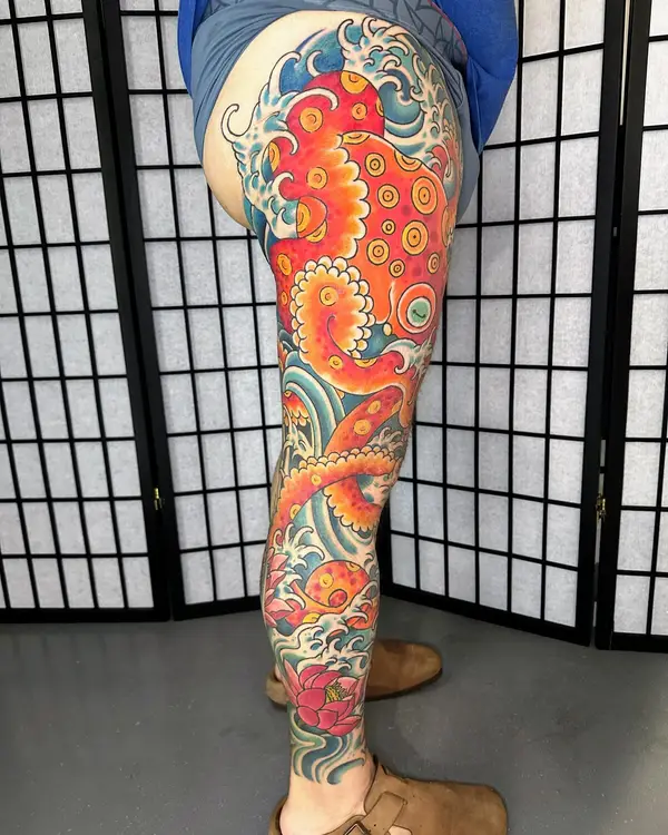 A Japanese-style color tattoo of an octopus and lotus among waves on a leg
