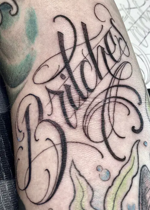 A fine-line script tattoo reading Britches