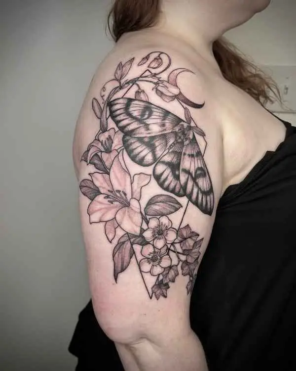 A black and grey tattoo of a moth, lilies, and a crescent moon