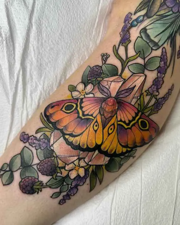 A color tattoo of a moth with orange and purple wings on crystals, lavender, and berries, by Jordan Joyes