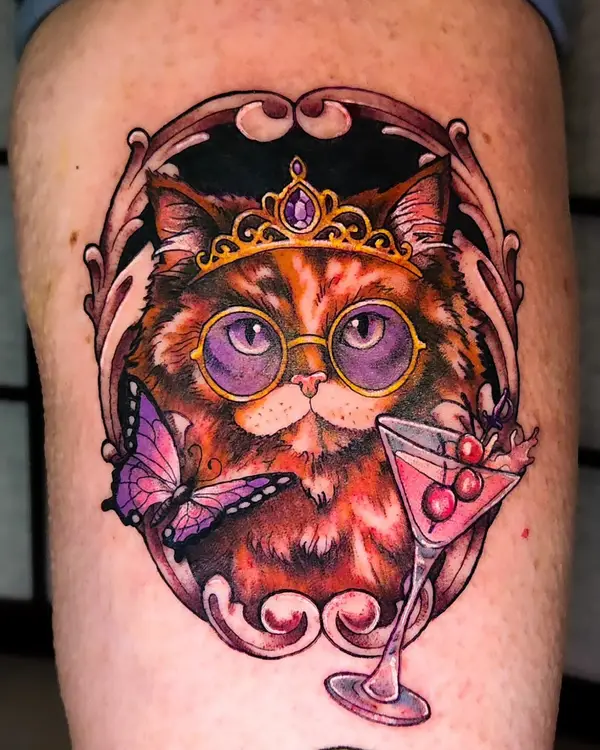 A color tattoo of a fluffy cat in a gold crown and purple glasses, with a butterfly and a cherry cocktail, by Amanda Boyd