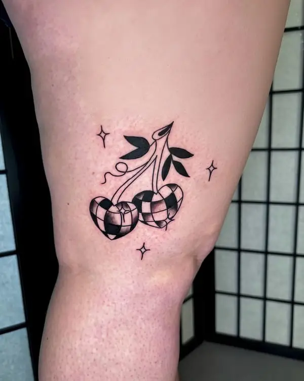 A black and grey tattoo of checkered heart-shaped cherries with leaves and stars, by Kate Elvey