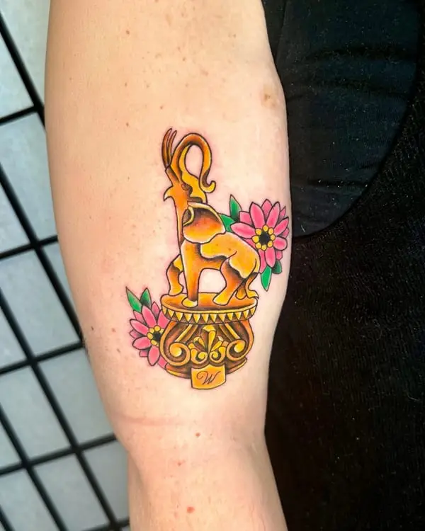 A color tattoo of a gold elephant on a pedestal with pink flowers, by Kate Elvey