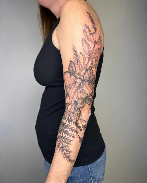 A fine-line black tattoo of a luna moth, leaves, and ferns on an arm