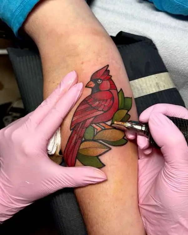 A color tattoo of a red cardinal on green and gold leaves, by Amanda Boyd