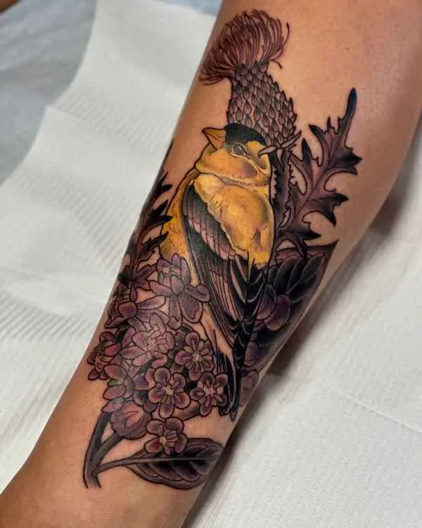 A neo-traditional tattoo of a yellow goldfinch perched on a thistle