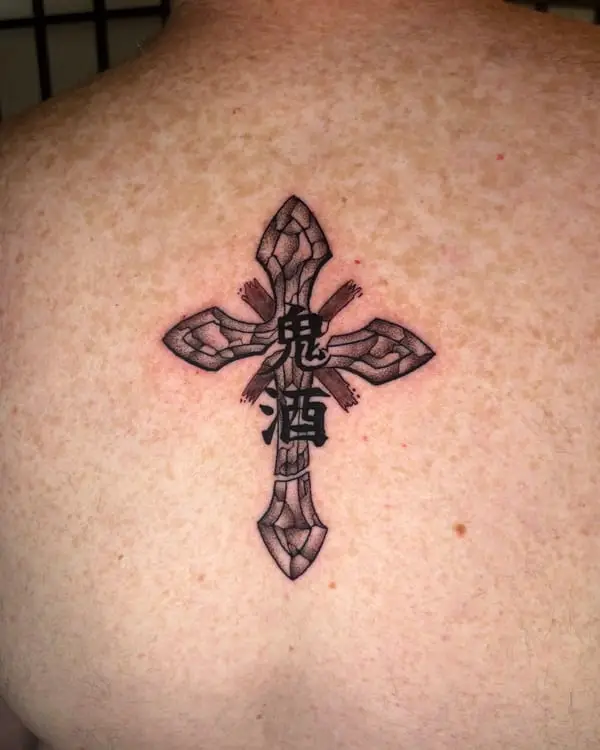 A black and grey tattoo of a stone-textured cross with kanji and wood beams, by Kate Elvey