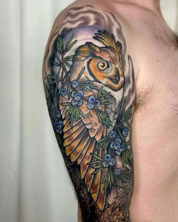 A color tattoo of an owl on evergreen branches with blue berries