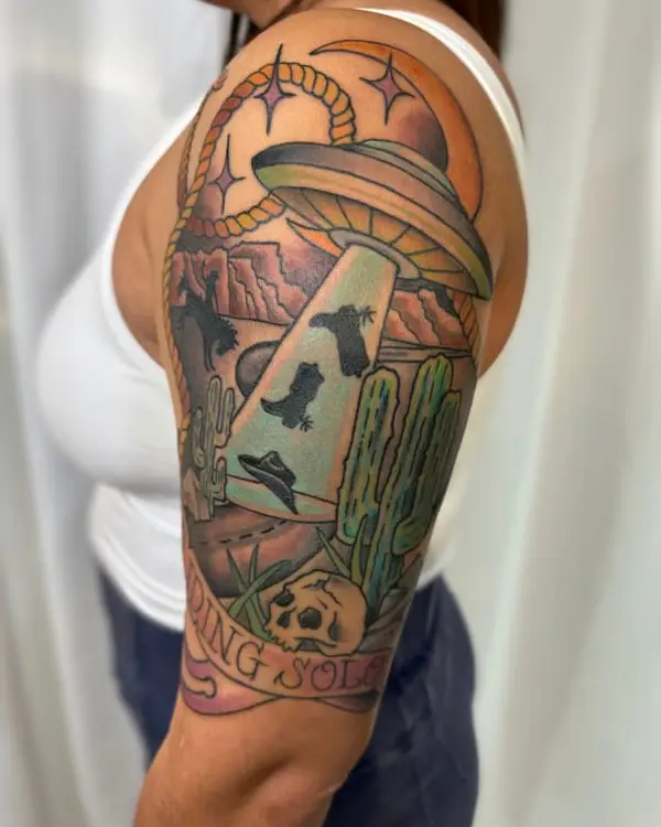 A neo-traditional tattoo of a UFO lifting cowboy gear over desert cacti, with a Riding Solo banner, by Betty Rose