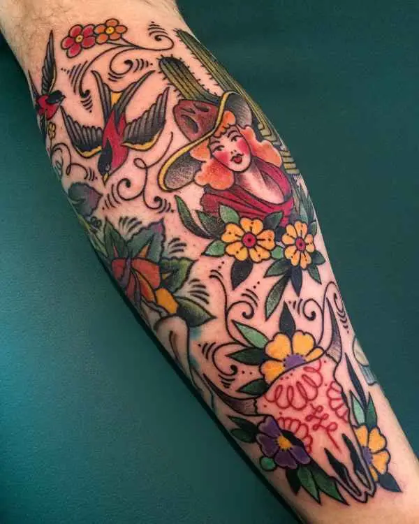 A colorful neo-traditional forearm tattoo of a cowgirl, swallows, cacti, and a decorated cow skull, by Betty Rose