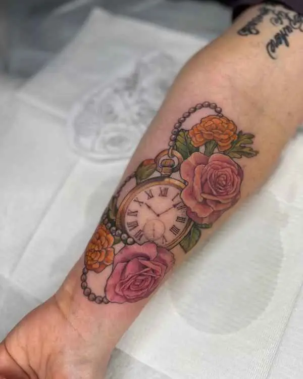 A color forearm tattoo of a gold pocket watch with pink roses and orange flowers