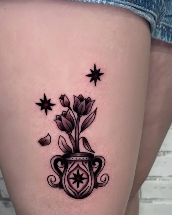 A black and grey tattoo of tulips in an ornate vase on a thigh, by Kate Elvey