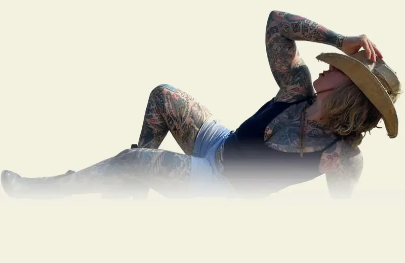 A relaxed client showing colorful tattoos, lying back with a cowboy hat